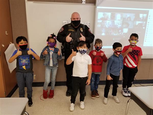 A police officer smiling with kids in front of a classroom.