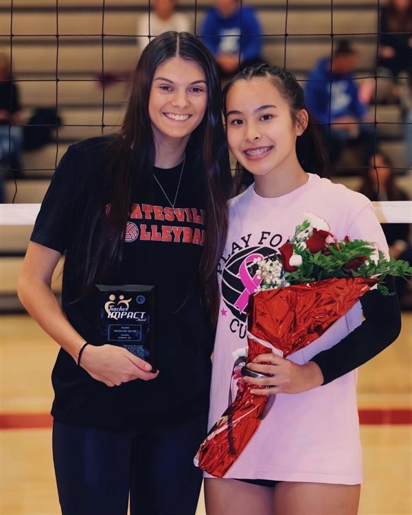 Two young women smiling and holding flowers while standing side by side.