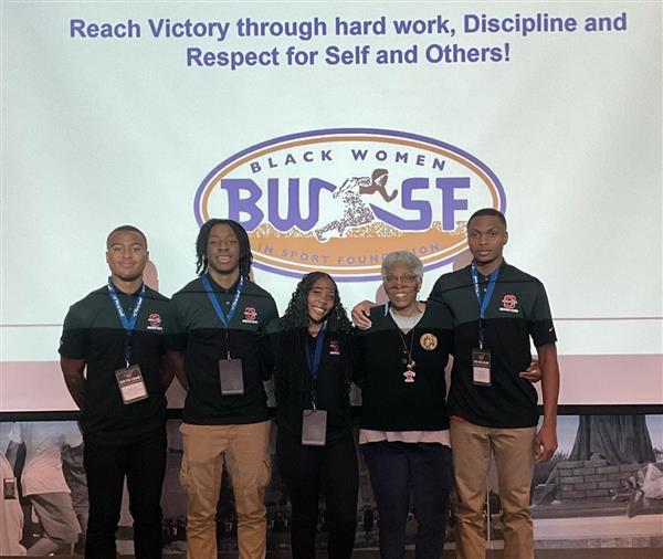 Five young individuals standing in front of a presentation screen.