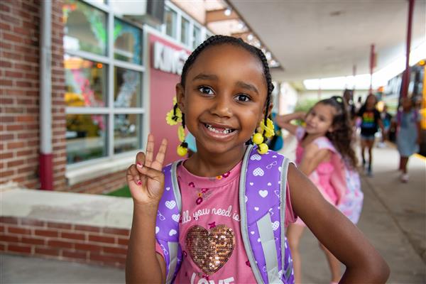 A young girl smiling while holding a backpack.