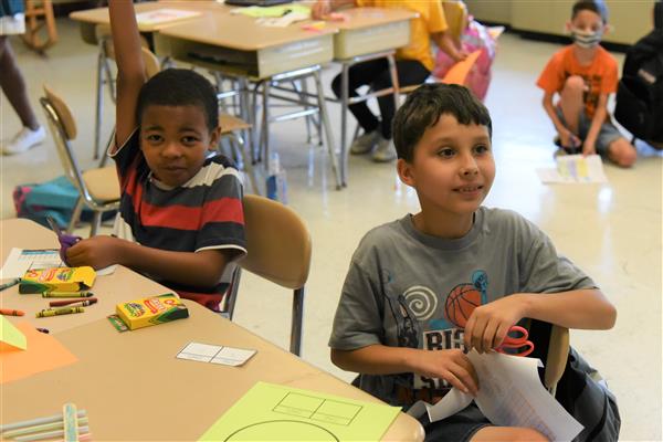 Two boys with hands raised in classroom, eager to participate in discussion.