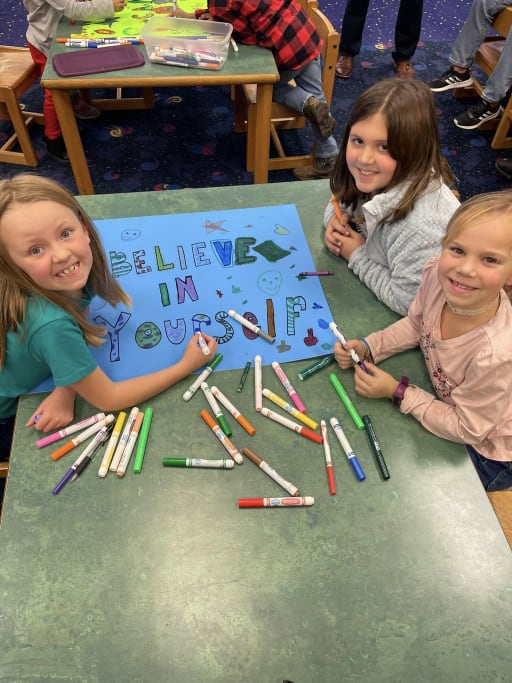 students making a sign and smiling at the camera