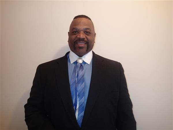 Professional man in formal attire standing against a white background.