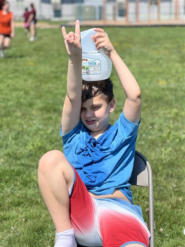 Boy sitting on folding chair holding water bottle.