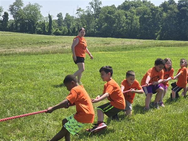 Children in orange shirts playing tug of war.