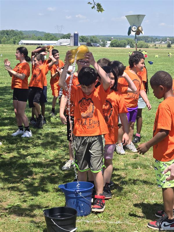 Children in orange shirts standing around a bucket.