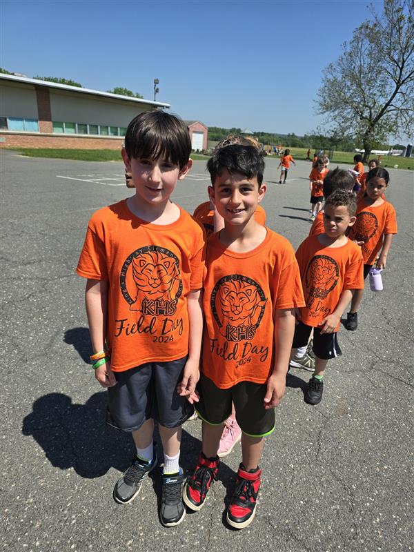 Children in orange shirts standing in parking lot.