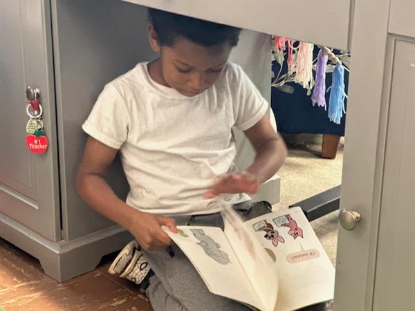 Young boy sitting on floor, reading book.