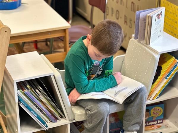 A young boy reading a book in a classroom.