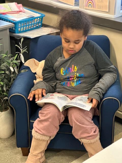  Young girl reading a book while sitting in a chair.