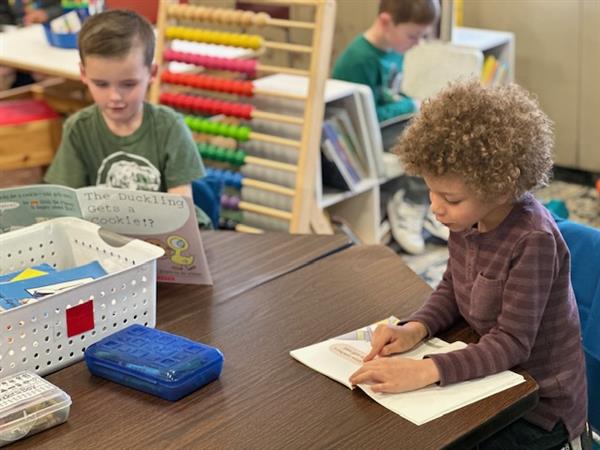 Two children sitting at a table with books and a box.