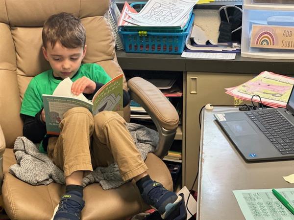 A young boy sitting in a chair, engrossed in reading a book.