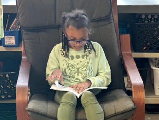 A young girl sitting in a chair reading a book.