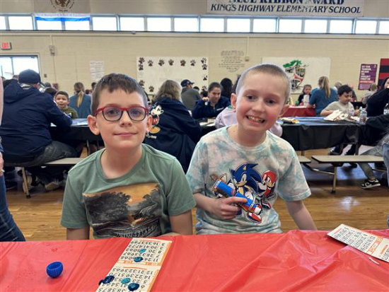 Two boys sitting at a table with a red and white tablecloth.