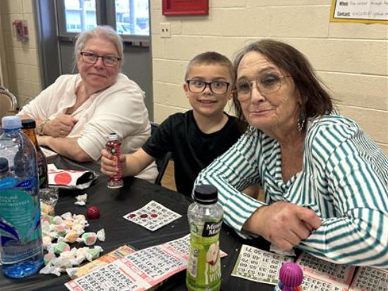 Two women and a boy sitting at a table playing bingo.