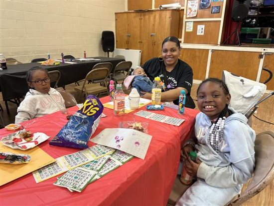 Three kids with adults at a table.