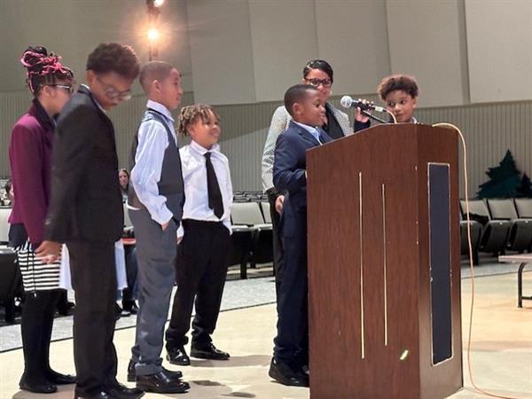 Children standing at podium, smiling and holding hands, ready to give a presentation.