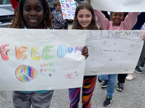 Three girls holding signs with the words "freedom" and "peace".