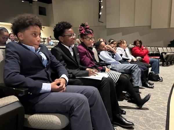 A group of people sitting in a room with their hands on their lap.