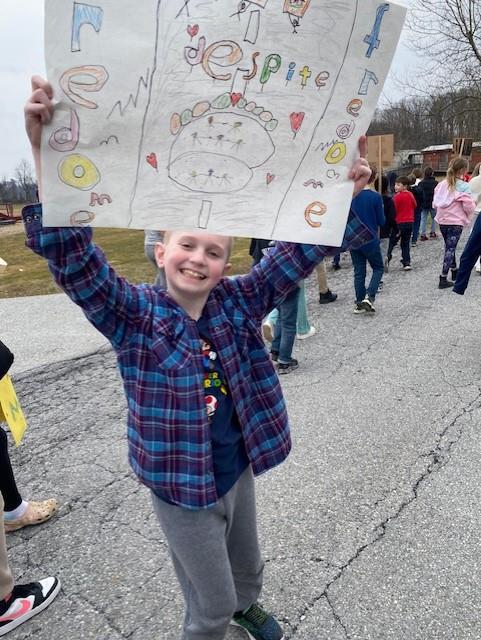 A young boy smiling and holding up a sign that says "love".