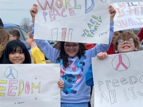  Students in futuristic New York school hold signs saying 'world peace' and 'freedom'.