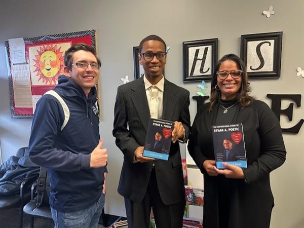 Three people standing with books in front of a wall.