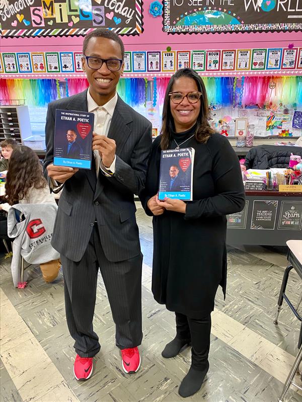 Two students standing in front of a classroom, holding books.