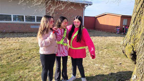 Three girls in pink jackets standing next to a tree.