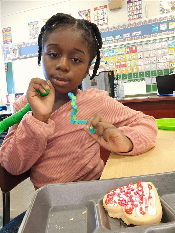 A young girl enjoying a cookie at a desk.