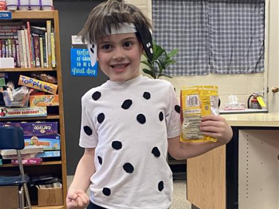 A boy in a polka dot shirt holding a bag of chips.