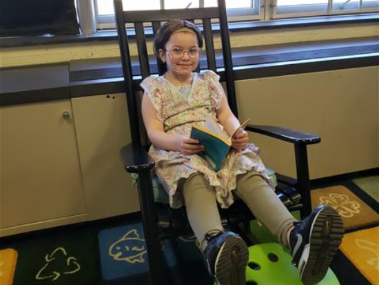  A young girl reading a book in a rocking chair.