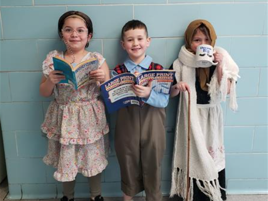 Three kids in costumes holding books.