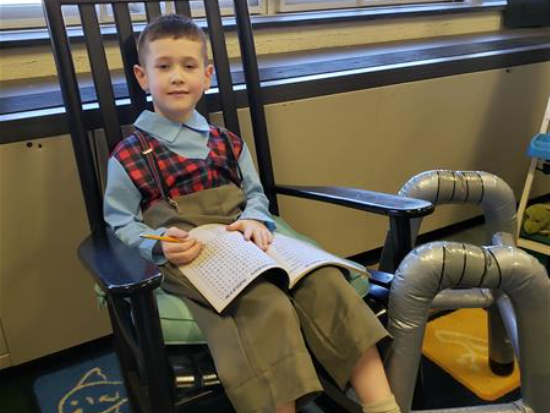 A boy reading a book while sitting in a rocking chair.