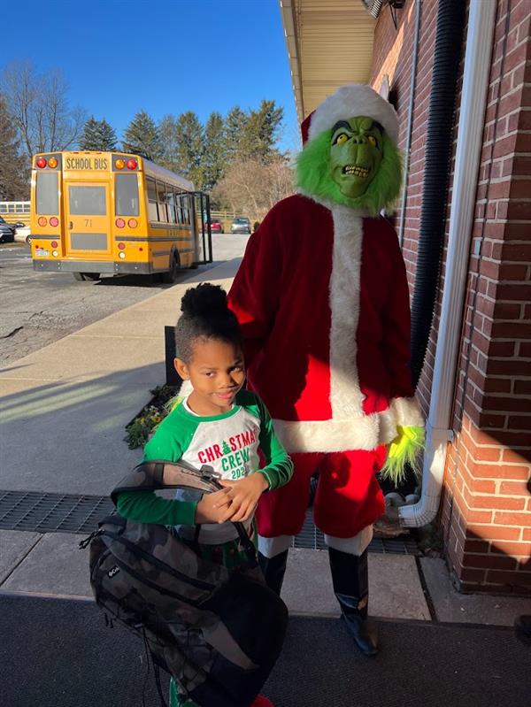 Children standing around a man dressed as the Grinch at a holiday event.