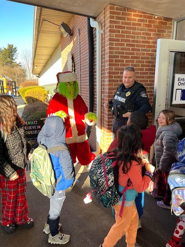 Children standing around a man dressed as the Grinch at a holiday event.