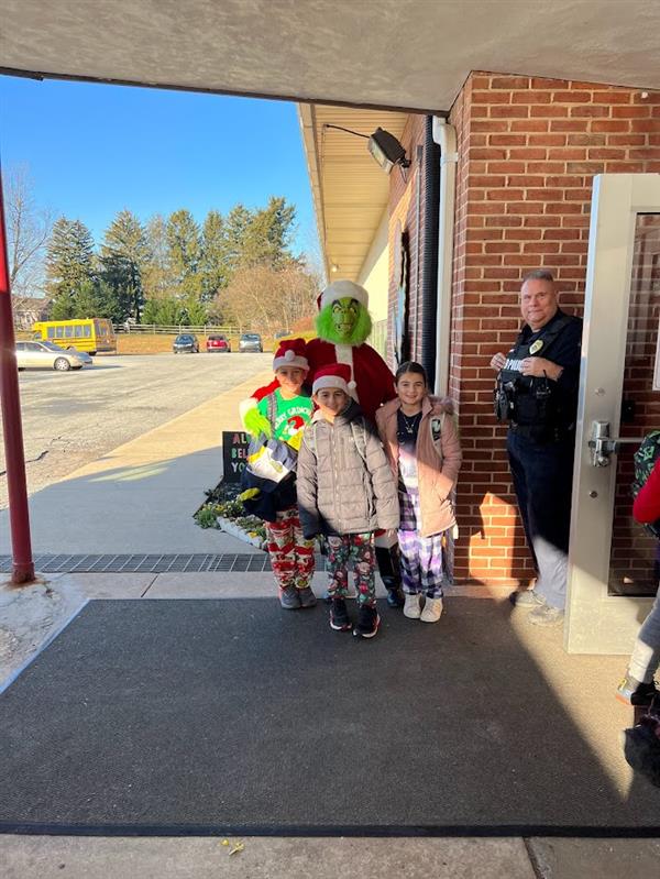 Children standing around a man dressed as the Grinch at a holiday event.