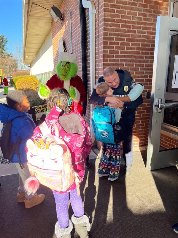 Children standing around a man dressed as the Grinch at a holiday event.