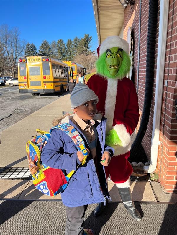 Children standing around a man dressed as the Grinch at a holiday event.