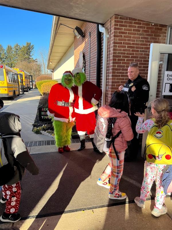 Children standing around a man dressed as the Grinch at a holiday event.