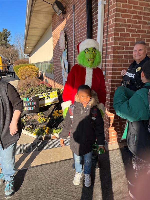 Children standing around a man dressed as the Grinch at a holiday event.