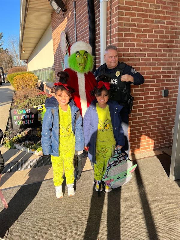 Children standing around a man dressed as the Grinch at a holiday event.