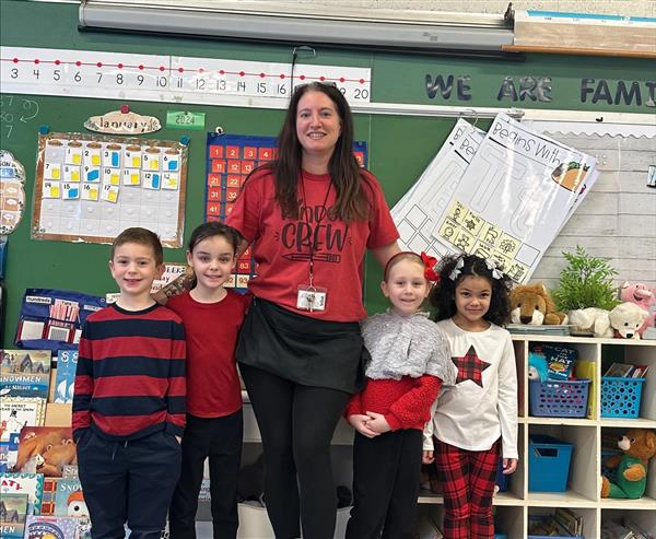 A teacher and her students smiling in front of a classroom.