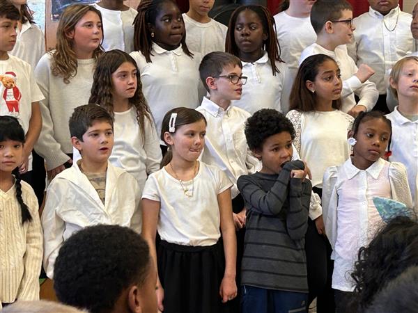 Group of students in white shirts and ties smiling for a photo in a hallway.