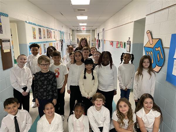 Group of students in white shirts and ties smiling for a photo in a hallway.