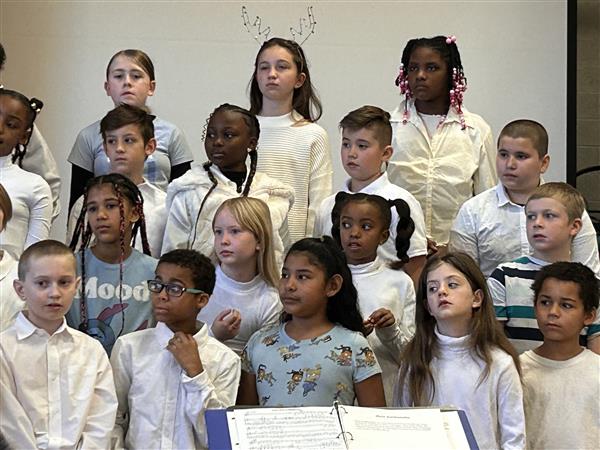 Group of students in white shirts and ties smiling for a photo in a hallway.