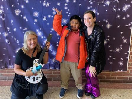 Three people smiling and posing with a guitar.