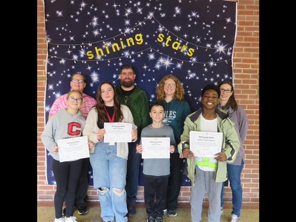 Children proudly display certificates in front of a wall.