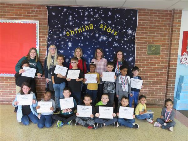 Children proudly display certificates in front of a wall.