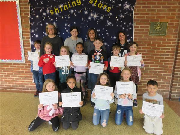 Children proudly display certificates in front of a wall.