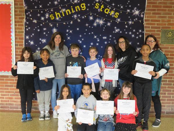 Children proudly display certificates in front of a wall.